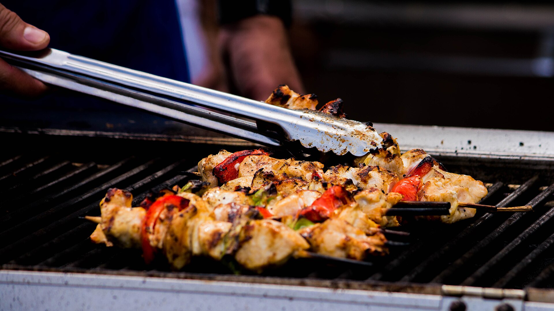 A cook turning chicken kebab skewers with peppers on a Mediterranean grill